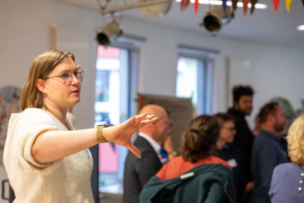eine frau moderiert mit ausgestreckter hand eine diskussion in einer stehenden gruppe eine frau moderiert mit ausgestreckter hand eine diskussion in einer stehenden gruppe