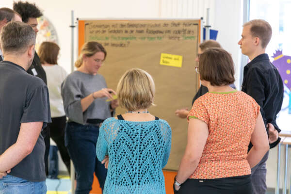 mehrere personen stehen vor einer pinnwand und arbeiten gemeinsam mit moderationskarten mehrere personen stehen vor einer pinnwand und arbeiten gemeinsam mit moderationskarten